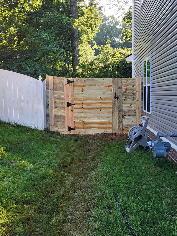 Wood double gate closing off a side yard between a house and a white fence