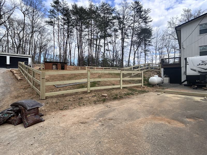 Three-rail wood fence with wire mesh backing around a yard